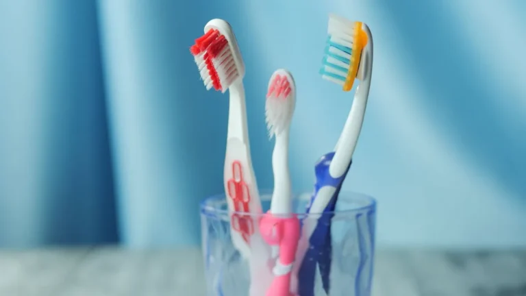 A trio of vibrant toothbrushes in a glass on a blue background, emphasizing dental hygiene.