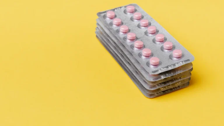From above set of small round pink pills packed in blisters on top of each other on yellow surface