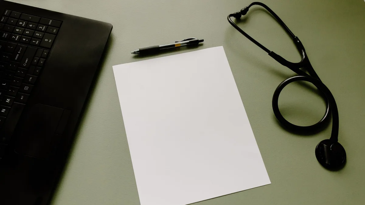 Professional workspace featuring a laptop, stethoscope, pen, and paper sheet for healthcare tasks.