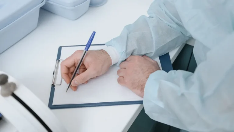 A medical professional wearing protective clothing writing on a clipboard.