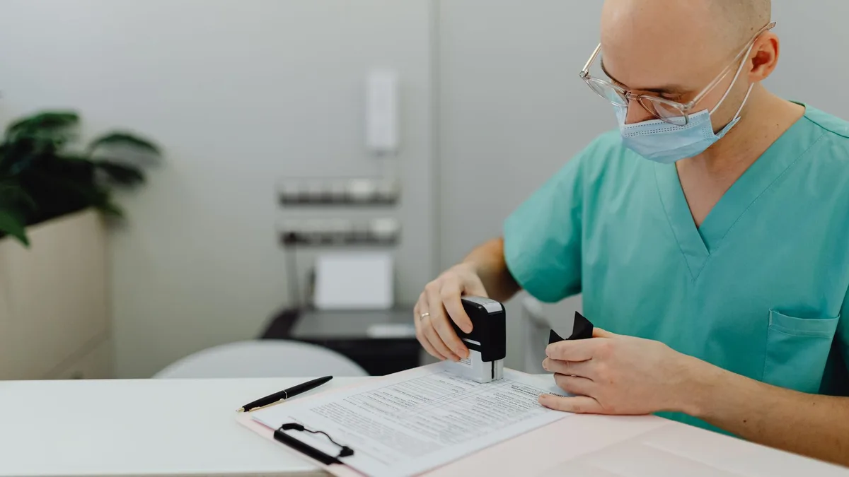 Medical professional in scrubs reviewing documents at an office desk.