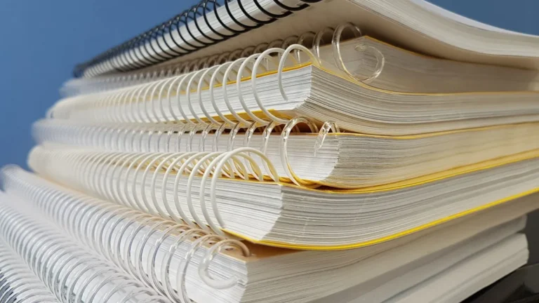 Close-up of stacked spiral notebooks with varied bindings against a blue backdrop.