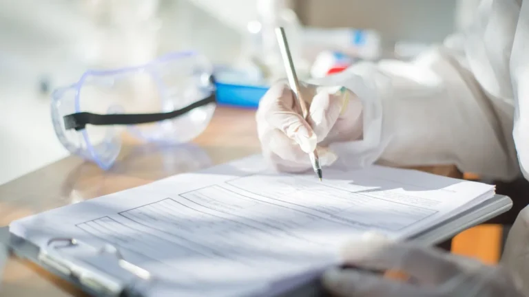 Close-up of a scientist writing on a document with gloved hands in a laboratory setting.
