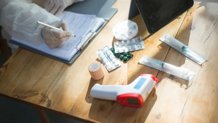 Medical practitioner filling forms with various medical items on desk, showing healthcare preparations.