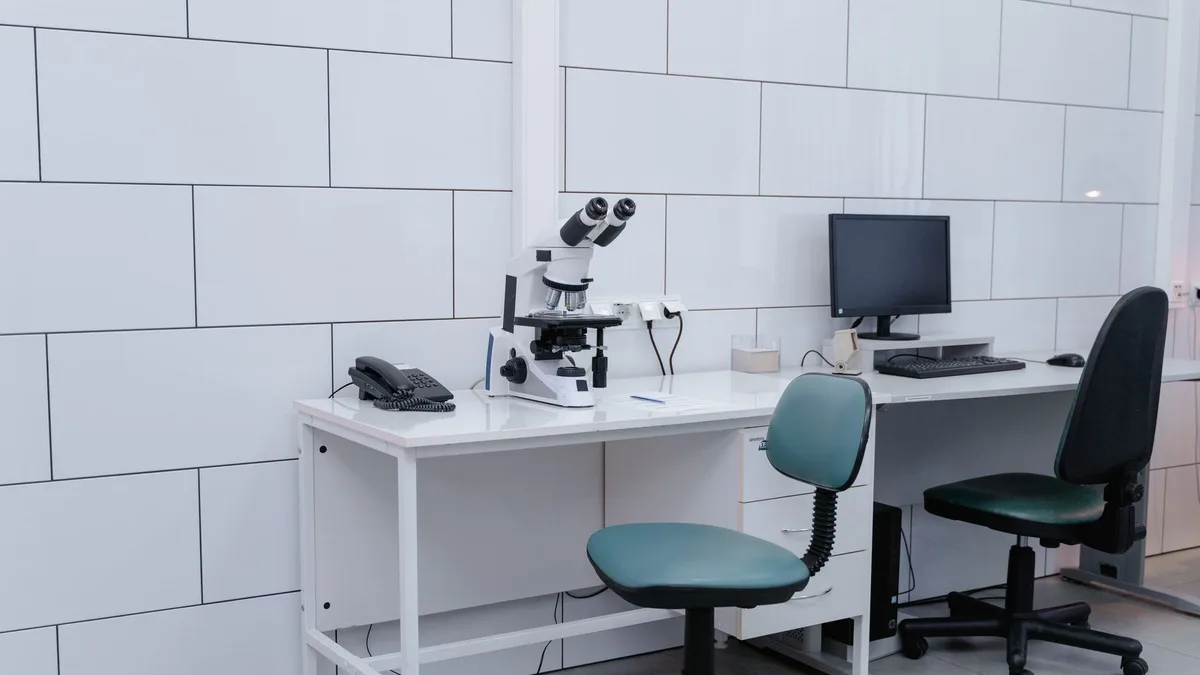 Modern laboratory with microscope, monitor, and office equipment on desk.