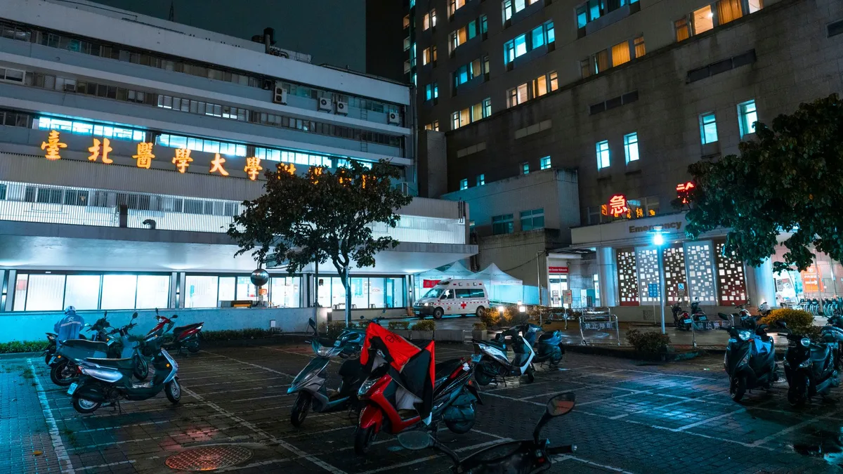 Night view of a hospital with scooters parked outside, illuminated by bright city lights.