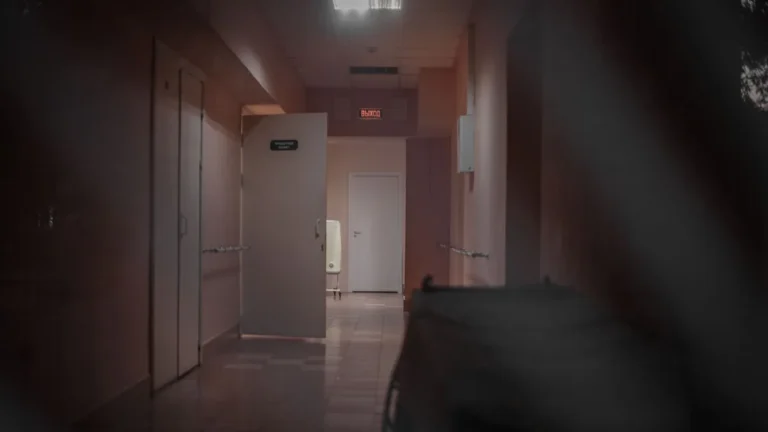 A deserted hospital corridor with open doors and dim lighting, enhancing a mysterious ambiance.